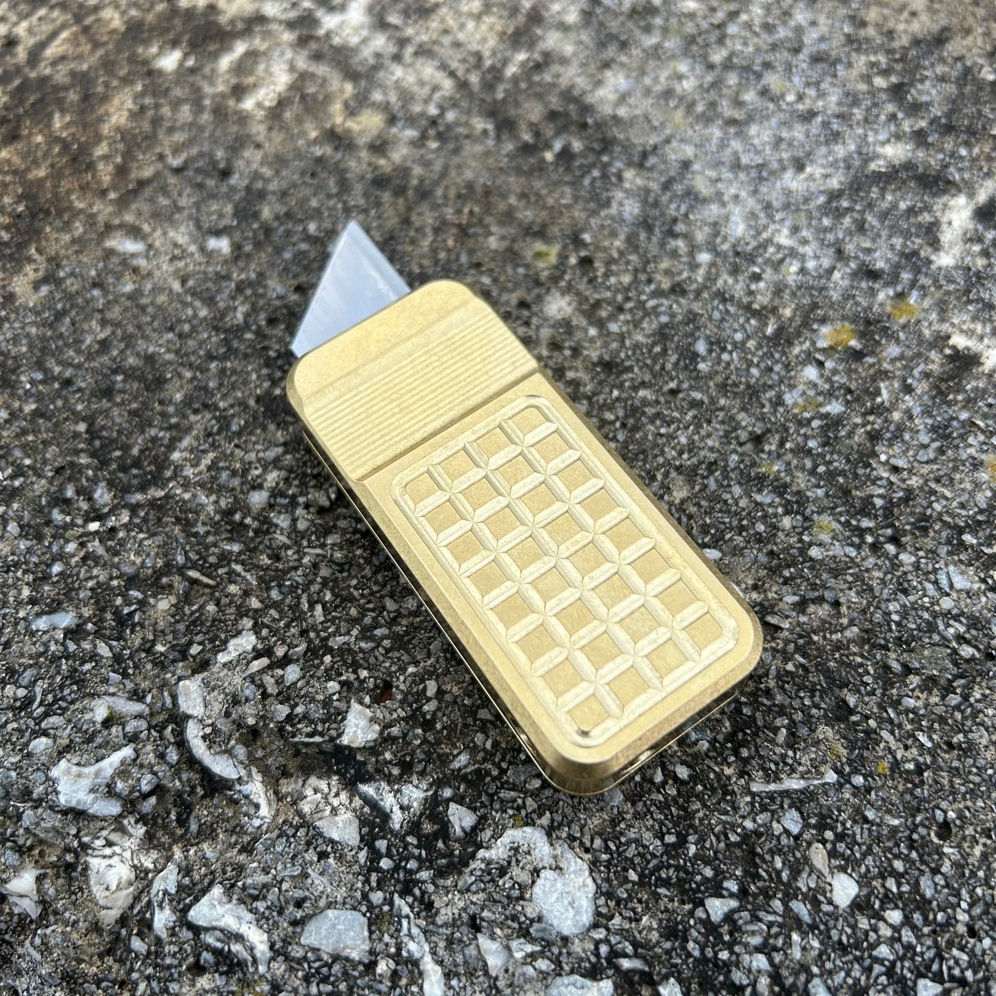 Brass Zero utility knife in a v2 grenade milling pattern with a stone background