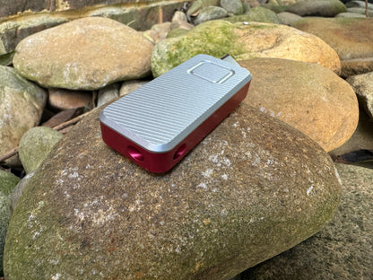 Red base and gray lid RiveryMFG Zero custom combinations utility knife with extended blade on stones.